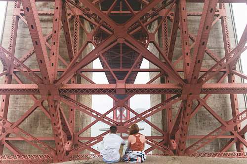 san francisco man and woman sitting near red metal scaffolding during daytime underneath